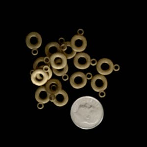 May include: A pile of gold-colored metal jump rings, some with a single loop at the top, others with two loops. The rings are scattered on a black surface.