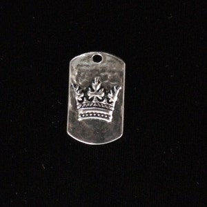 May include: Silver charm in the shape of a dog tag with a crown design.
