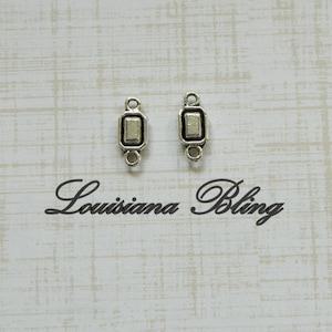 May include: Two silver-toned metal connector charms with a rectangular shape and a black outline. Each charm has a small loop on each side.