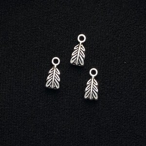 May include: Three silver leaf-shaped charms with a loop at the top for attaching to jewelry or other crafts.
