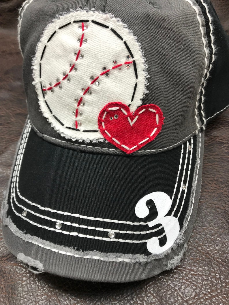 May include: Gray baseball cap with a white baseball and red heart applique. The cap has a black brim and the number 3 is embroidered on the front.