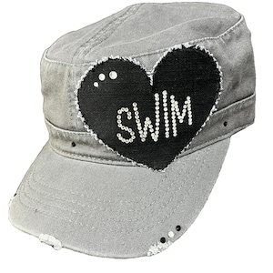 May include: A grey distressed denim baseball cap with a black heart-shaped patch that says "SWIM" in rhinestones.