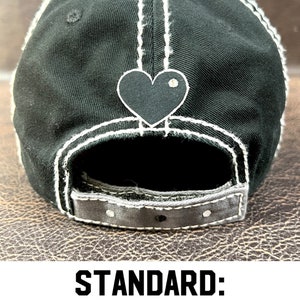 May include: Black baseball cap with white stitching and a black heart on the back. The back closure has rhinestones.