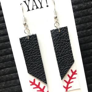 May include: A pair of black and white leather earrings with a red baseball stitch design. The earrings are on a white card with the text "YAY!" and "It's Gameday".