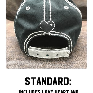 May include: Black baseball cap with white stitching and a black heart with a rhinestone on the back. The cap has a gray adjustable strap with rhinestones.