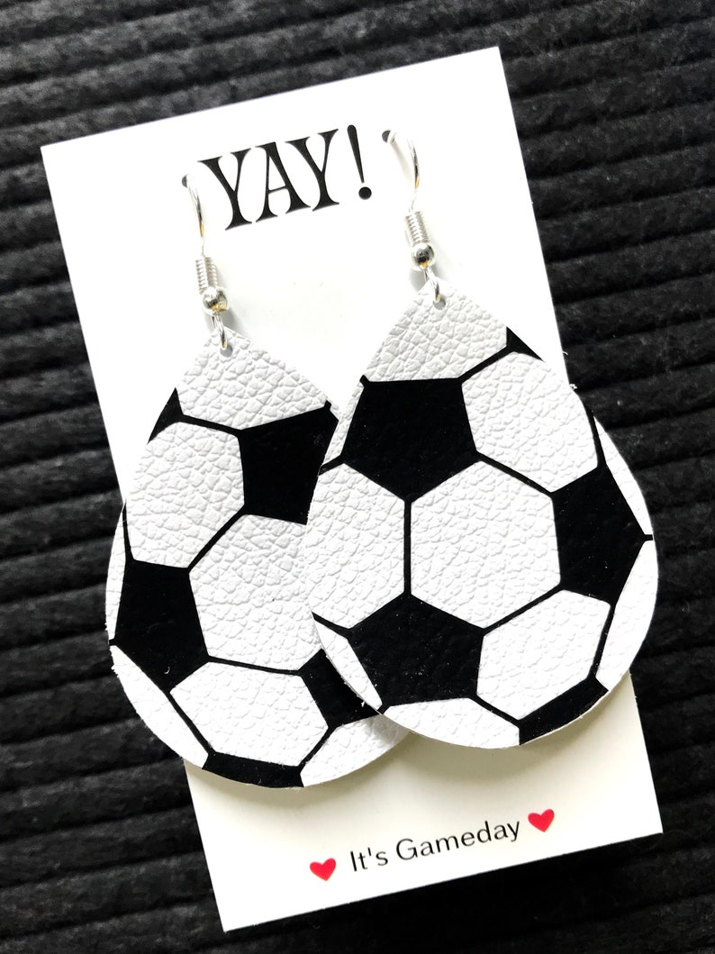 Peut inclure: Une paire de boucles d'oreilles pendantes en forme de ballon de football blanc et noir avec des crochets argent&eacute;s. Les boucles d'oreilles sont sur une carte blanche avec le texte "YAY!" et "It's Gameday" en noir et rouge.