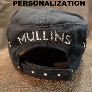 May include: Black cotton baseball cap with a black strap and rhinestones. The cap has the word "MULLINS" written in rhinestones on the back.