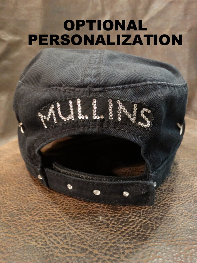 May include: Black cotton baseball cap with a black strap and rhinestones. The cap has the word "MULLINS" written in rhinestones on the back.