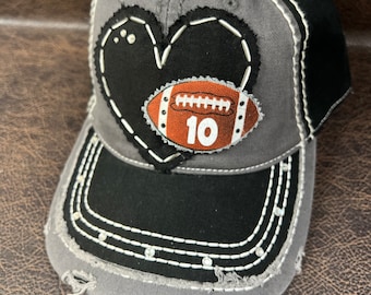 Può includere: Cappellino da baseball grigio e nero con un cuore nero e un pallone da calcio marrone con il numero 10. Il cappello ha cuciture bianche e strass.