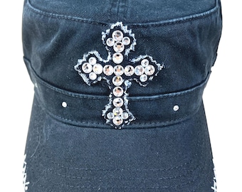 Puede incluir: Una gorra de estilo militar de denim negro con una gran cruz de pedrería en la parte delantera. La cruz es plateada con pedrería transparente.