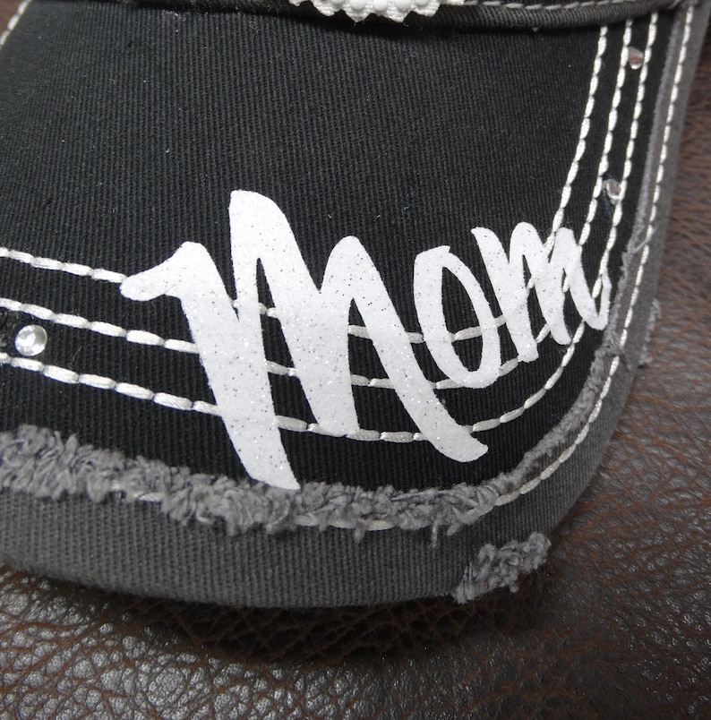 May include: Black baseball cap with a gray brim and white glitter lettering that says "Mom".