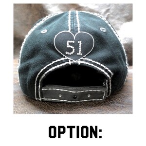 May include: Black baseball cap with a white heart-shaped patch that says "51" in rhinestones. The cap has a white stitching detail around the brim.