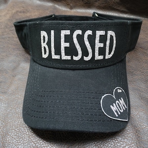 May include: Black visor with a silver glitter 'BLESSED' inscription and a silver glitter heart with 'MOM' inside.