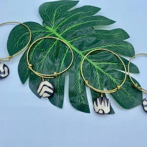 Könnte beinhalten: Vier goldene Armreifen mit runden Anhängern in Schwarz-Weiß-Muster. Die Anhänger haben verschiedene geometrische Designs.