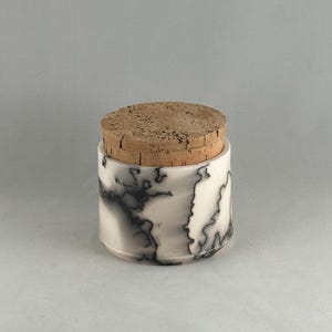 May include: A white ceramic jar with a black lightning pattern and a cork lid. The jar is cylindrical and has a smooth, glossy finish. The cork lid is round and fits snugly on top of the jar.