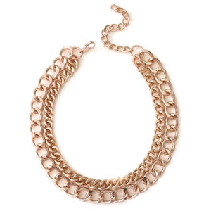 Puede incluir: Un collar de cadena de capas de tono dorado con tres estilos de cadena diferentes. El collar está hecho de metal y tiene un cierre de mosquetón.