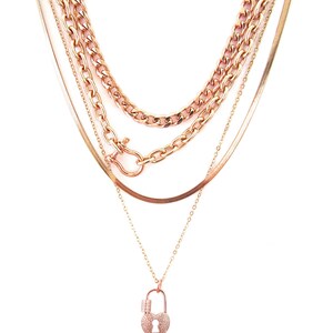 May include: A layered rose gold necklace with a heart-shaped padlock pendant. The pendant is adorned with small sparkling stones.