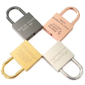 May include: Four engraved padlocks in different colors: silver, gold, rose gold, and black. The padlocks have various romantic messages engraved on them, including "You're stuck with me." and "Locked in Love."