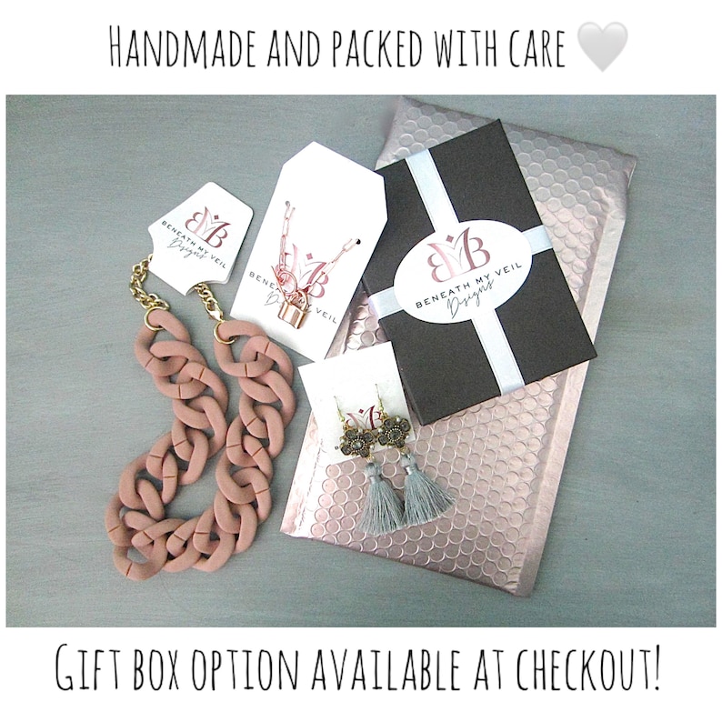 May include: A pink bubblegum chain necklace, gray tassel earrings, and a gift box with a white ribbon and the text "Beneath My Veil Designs" are displayed on a pink bubble wrap envelope. The text "HANDMADE AND PACKED WITH CARE" and a heart emoji are at the top of the image. The text "GIFT BOX OPTION AVAILABLE AT CHECKOUT!" is at the bottom of the image.