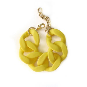 Puede incluir: Un brazalete de cadena gruesa de color amarillo con un cierre dorado.