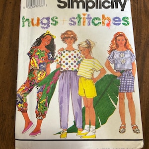May include: A Simplicity 7725 sewing pattern envelope for size AA (7-10) titled Hugs + Stitches. The front features illustrations of four outfits: a floral print set, a polka dot top with purple pants, a striped top with yellow shorts, and a gingham set.