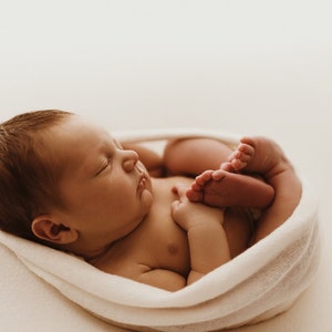 Newborn baby wrapped tightly in white newborn stretch wrap, resting on white blanket. Newborn photography session.