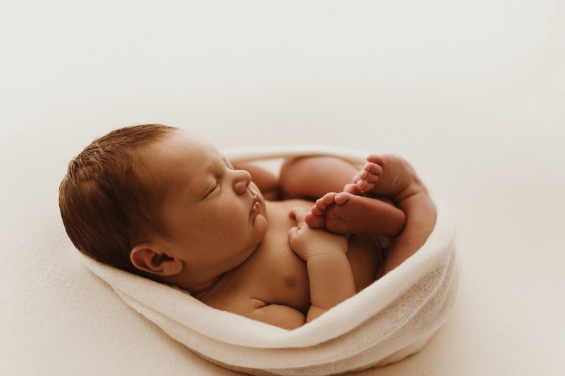 Newborn baby wrapped tightly in white newborn stretch wrap, resting on white blanket. Newborn photography session.