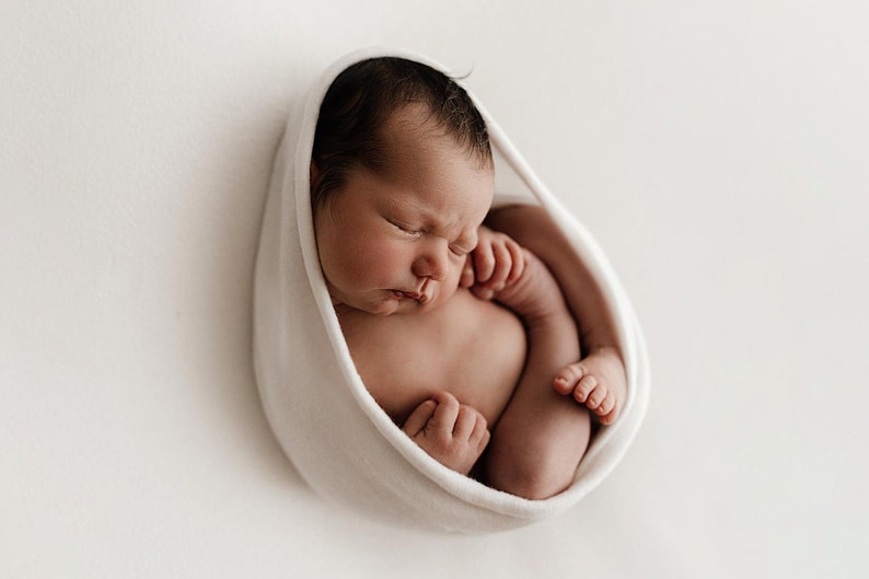Newborn baby wrapped tightly in white newborn stretch wrap, resting on white blanket. Newborn photography session.