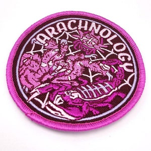 May include: A pink embroidered patch with the word "Arachnology" in a circle around a design of three pink spiders in a web.