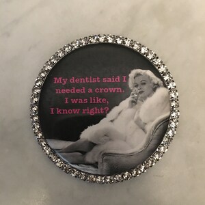 May include: A round, silver-colored pin with a rhinestone border. The pin features a black and white image of a woman in a fur coat with the text "My dentist said I needed a crown. I was like, I know right?"