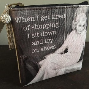May include: A black and white zippered pouch with a quote that reads "When I get tired of shopping I sit down and try on shoes". The pouch features a black and white photo of a woman sitting down and trying on shoes.