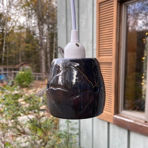 May include: A dark blue ceramic pendant light fixture with a white cord and a white socket. The light fixture has a textured surface and a starburst design.