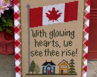 May include: Cross-stitch embroidery with a Canadian flag, houses, trees, and the text "With glowing hearts, we see thee rise!"