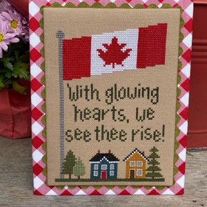 May include: Cross-stitch embroidery featuring a Canadian flag, houses, trees, and the text "With glowing hearts, we see thee rise!"