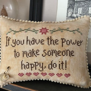 May include: A beige pillow with a brown embroidered quote: "If you have the power to make someone happy, do it!"  The pillow has a white pom-pom trim and a small pin with buttons on the side.