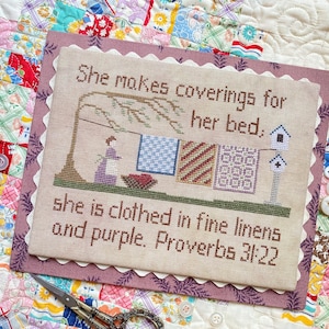 Może przedstawiać: Wzór haftowany krzyżykiem z wersetem z Księgi Przysłów 31:22: "Ona szyje okrycia na swoje łoże, ubiera się w drogie płótno i purpurę. Przysłów 31:22". Wzór przedstawia kobietę wieszającą kołdry na sznurze do suszenia.