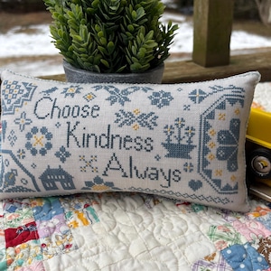 Könnte beinhalten: Ein weißes Kissen mit blauer und gelber Stickerei. Das Kissen zeigt den Text "Choose Kindness Always".