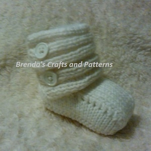 May include: White knitted baby booties with white buttons. Brenda's Crafts and Patterns.