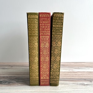 Puede incluir: Tres libros antiguos con cubiertas decorativas. Los lomos muestran títulos como "The Poems of John Keats" y "Little Dorrit by Charles Dickens". Los libros son de color verde y rojo con letras doradas.
