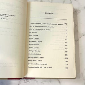 K&ouml;nnte beinhalten: Ein Buch mit dem Titel "Choice Homemade Cookies from Countryside America" mit einem Inhaltsverzeichnis, das verschiedene Arten von Keksen und die Seitenzahlen auflistet, auf denen sie zu finden sind.