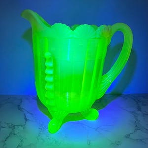 May include: A bright green glass pitcher with a fluted design and three legs. The pitcher has a scalloped rim and a handle.