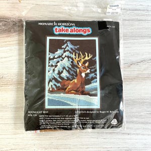 May include: A Monarch Horizons "take alongs" needlepoint kit, featuring a deer resting in a snowy forest scene. The design size is approximately 5 x 7 inches. The kit includes yarn, canvas, needle, instructions, and stretcher bars.