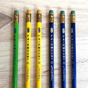Könnte beinhalten: Sechs Bleistifte in Grün, Gelb und Blau. Jeder Bleistift hat eine goldene Zwinge, einen rosa Radiergummi und den Text "2 FAIRMOUNT" vertikal aufgedruckt. Die Bleistifte sind von Empire Pencil Co. und hergestellt in den USA.