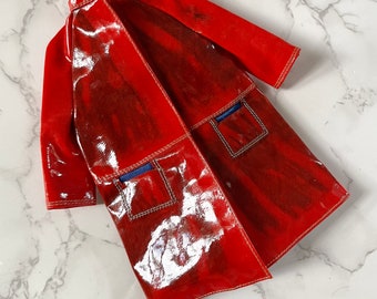 May include: A red, shiny, long coat with blue trim and two pockets. The coat has a collar and is made of a glossy material.