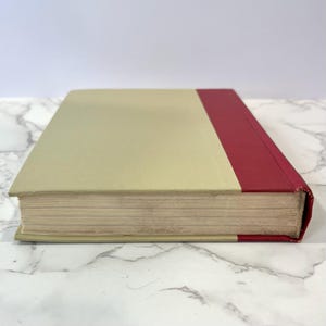 K&ouml;nnte beinhalten: Ein gebundenes Buch mit einem cremefarbenen Einband und einem roten R&uuml;cken.