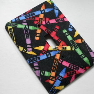 May include: A black light switch cover with a colorful crayon pattern. The crayons are labeled with the colors: blue, red, orange, yellow, green, purple, pink, and black.