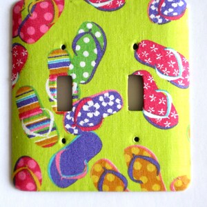 May include: A green light switch cover with a pattern of colorful flip flops. The cover has two switch openings.