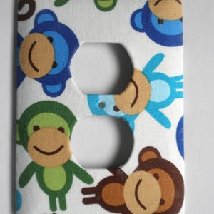 May include: A white outlet cover with a monkey pattern. The monkeys are blue, green, and brown with smiling faces.
