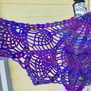 May include: A purple and blue crocheted shawl with a lacy pattern. The shawl is draped over a dress form.