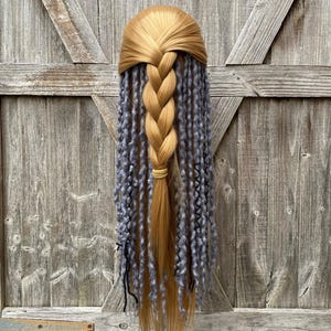 May include: A golden-blonde wig with a braided crown and a long, thick braid. The braid is secured with a light-colored band. The lower portion of the wig features long, gray, curly extensions, creating a unique and stylish look.